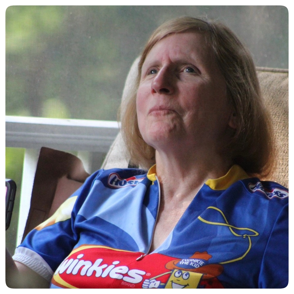 Karen Keninger, a white woman with light red hair is pictured in a candid shot. She is wearing a blue cyclist's jersey with the Hostess Twinkies logo across the front.